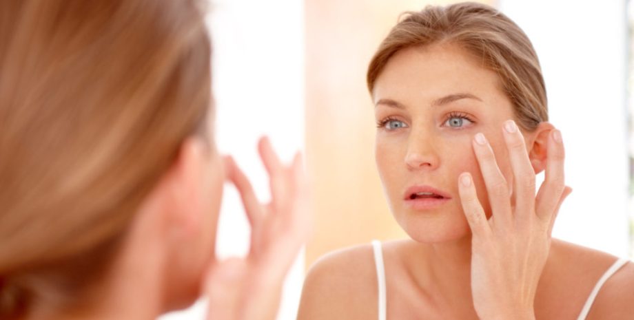 A woman looking into a mirror touching the skin below her eye.