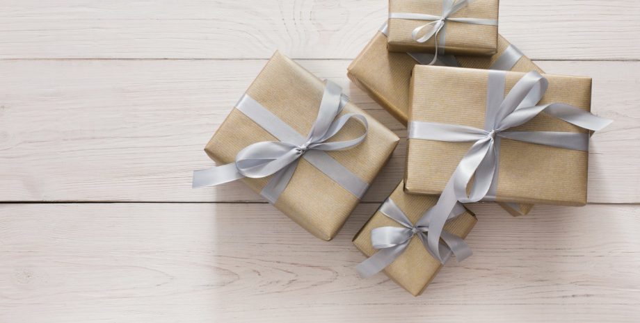 Top view of gift boxes on white wood background. Presents in craft paper decorated with stylish elegant silver satin ribbon bows.