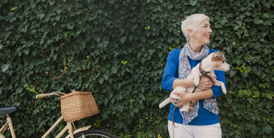 Beautiful mature woman holding dog, leaves behind them and bicycle