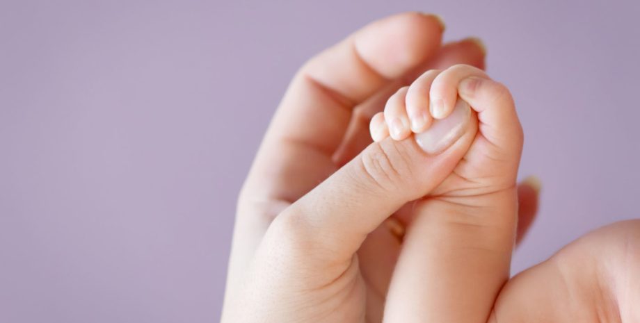 a baby's hand gripping it's mom's thumb