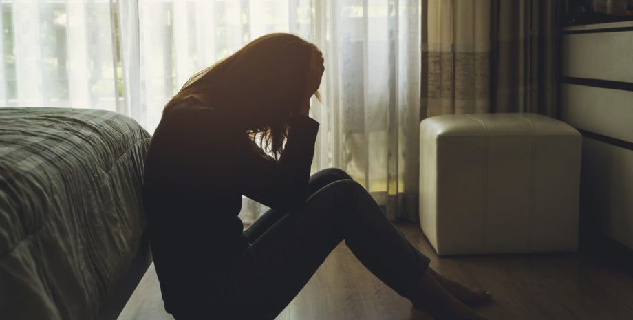 a woman sitting on the floor in a dark room with her hands on her head
