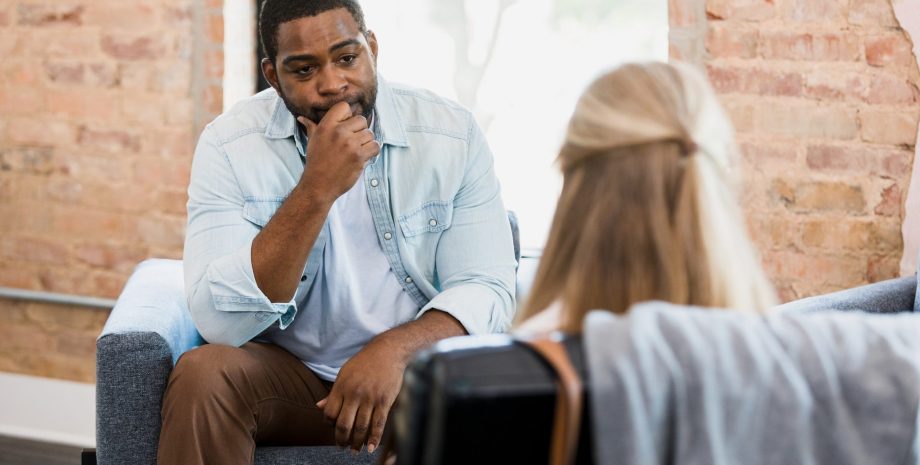 Exhausted mid adult man listens to unrecognizable female therapist