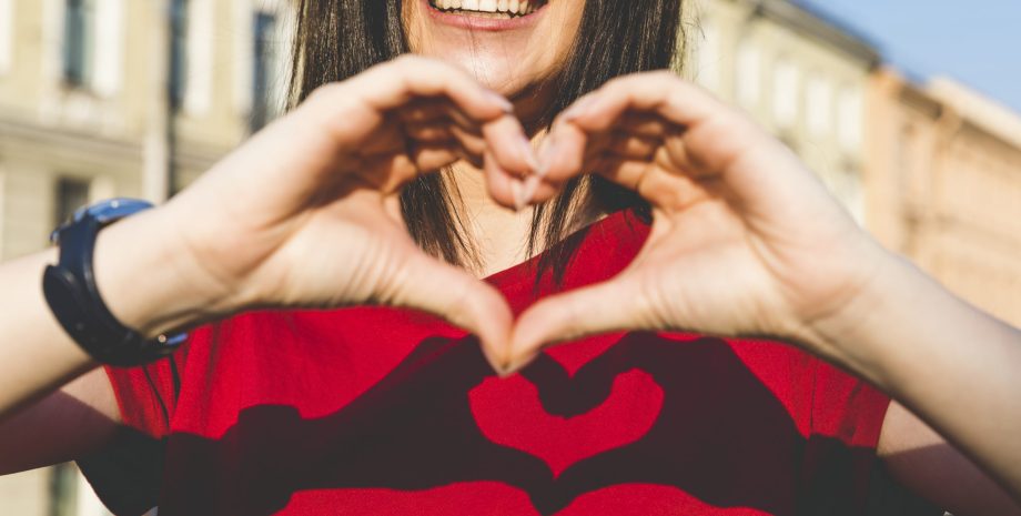 Woman's hands shaping heart, shadow on red t-shirt