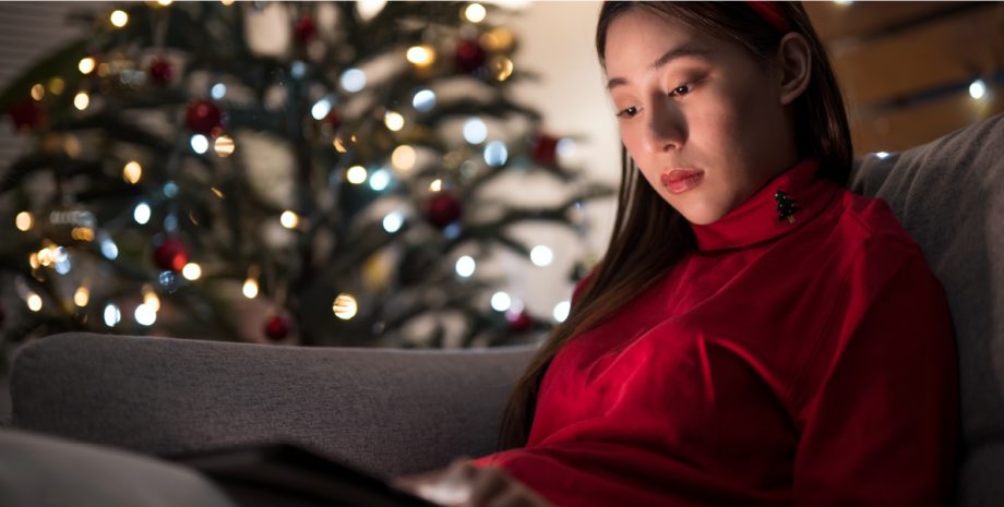 A woman on her laptop seated in front of a Christmas tree.