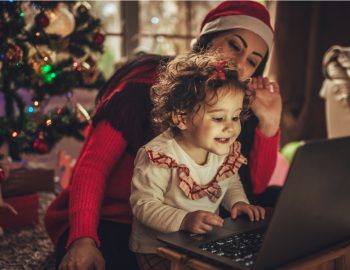 A mother and child use a computer in front of a Christmas tree.