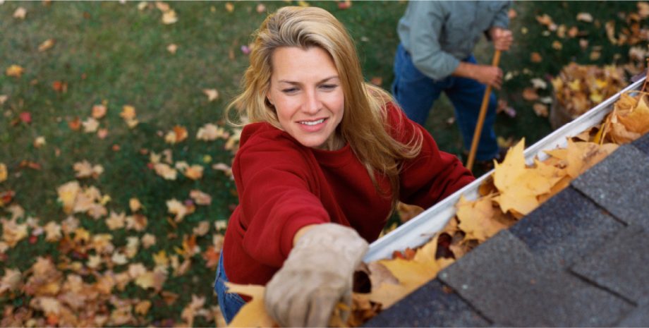 Woman cleaning her gutters on top of a ladder.
