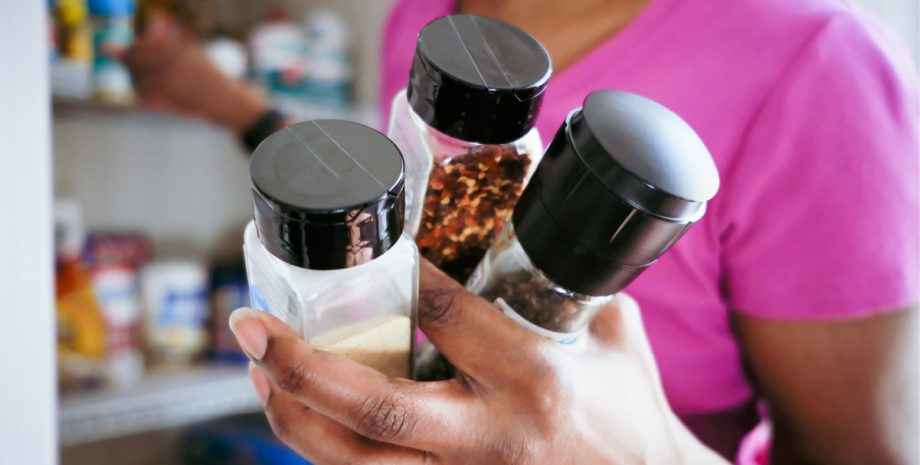 Someone holding three spice containers near the camera.