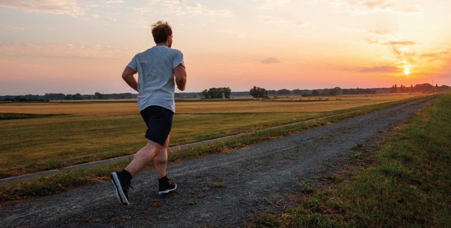A man running down a long gravel road toward a sunset.