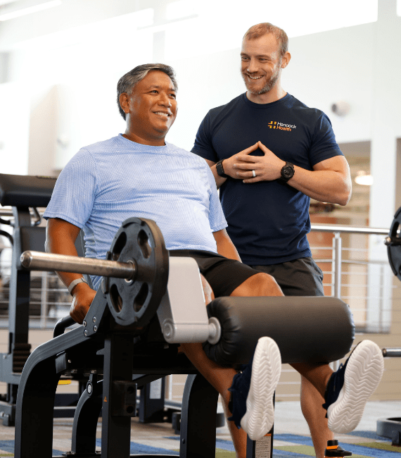 man and trainer lifting weights at a Hancock Wellness Center