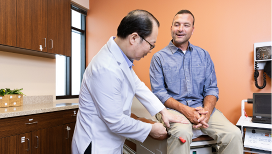 Smiling male patient getting a knee reflex examination by a Hancock Health doctor in an exam room