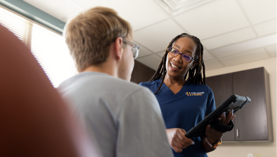Hancock Health nurse smiling with tablet and talking to patient in exam room