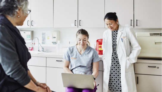 Female doctor and nurse reviewing patients chart on laptop during appointment in exam room