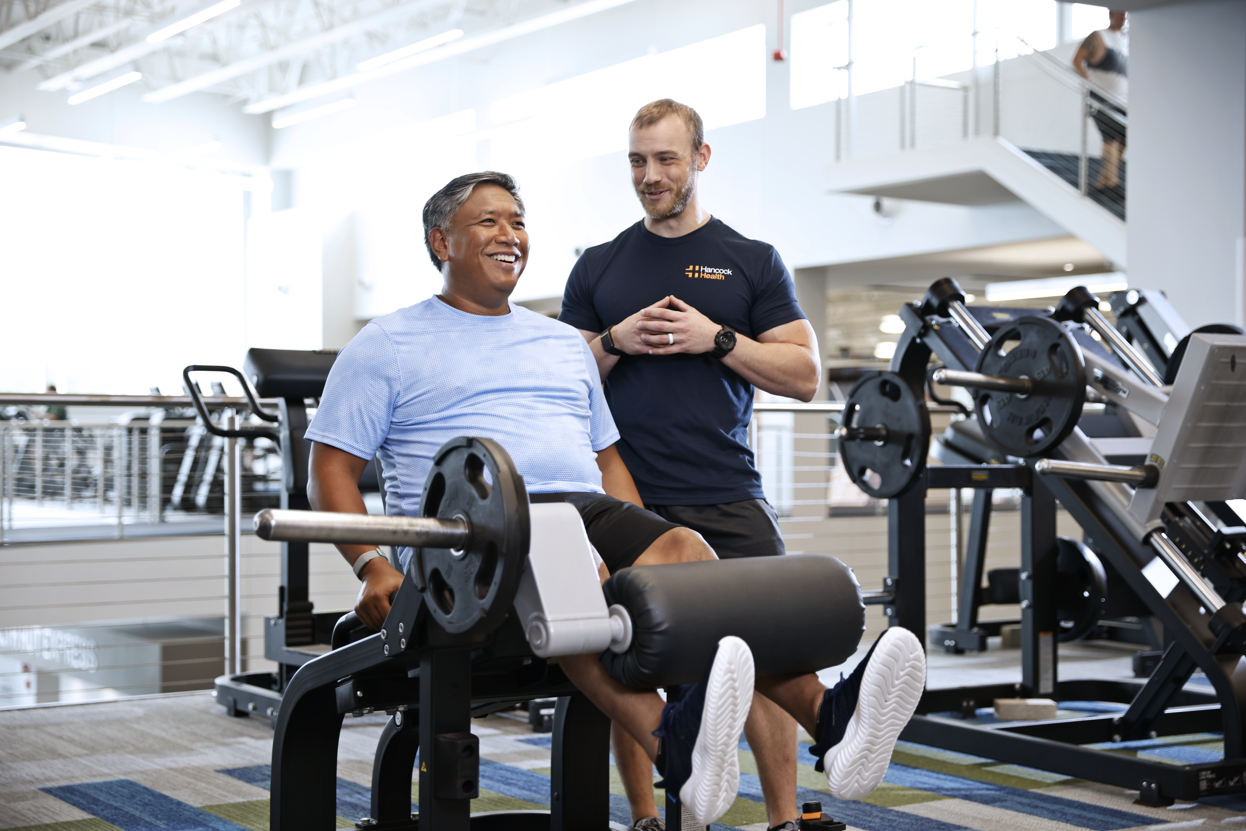 man and trainer lifting weights at a Hancock Wellness center