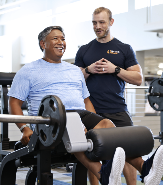 man and trainer lifting weights at a Hancock Wellness Center