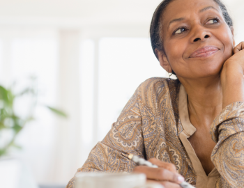A woman writing a list and looking off to the left as she smiles.